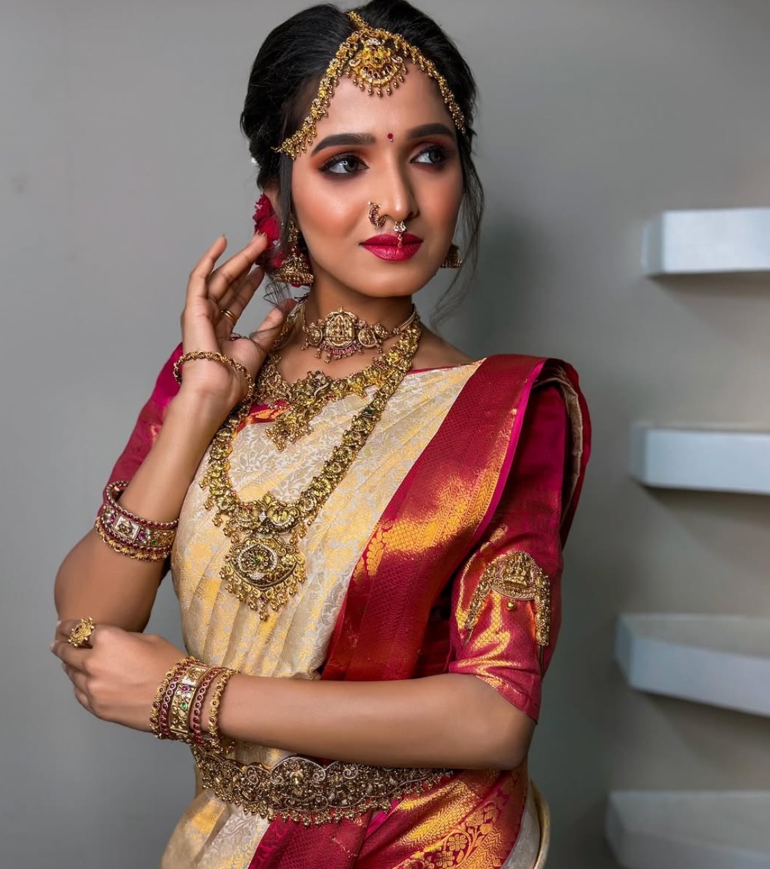 Bride in ivory gold Muhurtham saree with ruby-pink blouse featuring Lord Lakshmi temple arch sleeve embroidery